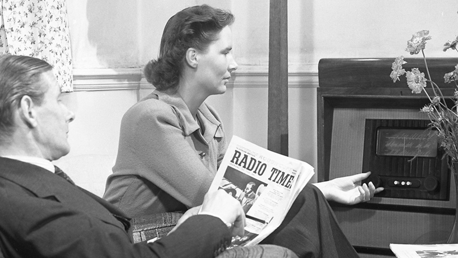 old photo of a man & woman listening to the radio. the man is holding a newspaper with the headline "Radio Time".