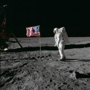 Astronaut standing on the surface of the moon next to the American flag.